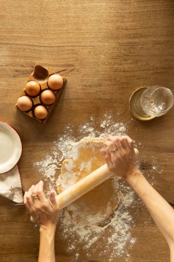 Ellerin hamuru yuvarlama görüntüsü un kaplı bir masanın üzerinde ahşap bir raptiye ile, çerçevesinde yumurta ve cam ile, kırsal bir mutfak düzeninde ev yapımı pişirme işlemi yakalamak.
