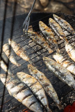 Kömür ızgarasında ızgara sardalya, altın, dumanlı deriyle geleneksel Portekiz mutfağının özünü yakalıyor. Bu sahne, ızgara sardalyanın ikonik bir yemek olduğu Portekiz 'deki yaz şenliklerinin otantik lezzetini çağrıştırıyor.