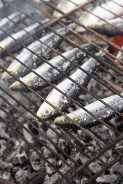 Kömür ızgarasında ızgara sardalya, altın, dumanlı deriyle geleneksel Portekiz mutfağının özünü yakalıyor. Bu sahne, ızgara sardalyanın ikonik bir yemek olduğu Portekiz 'deki yaz şenliklerinin otantik lezzetini çağrıştırıyor.