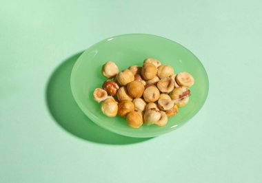  Pastel yeşil bir tabakta kavrulmuş fındıklı minimalist bir görüntü. Temiz ve canlı kurgu sağlıklı atıştırmalıkları ön plana çıkarıyor ve yeni ve modern bir görünüm yaratıyor.