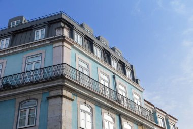 Göz kamaştırıcı bir Lizbon binası. Geleneksel Portekiz mimarisi. Pastel mavi bir cephe, zarif dövmeli demir balkonlar ve parlak mavi gökyüzüne karşı kurulmuş modern bir çatı..