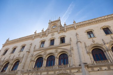 Stunning view of Rossio Station in Lisbon, showcasing its intricate neo-Manueline architectural details under a bright blue sky. A historic landmark and a must-see for visitors to Portugal. clipart