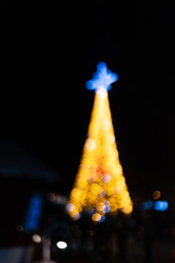 Artistic photograph of a Christmas tree with golden lights and a glowing blue star at the top. The soft bokeh effect creates a festive, magical atmosphere, perfect for holiday-themed designs. clipart