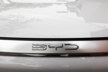 Modern elektrikli bir arabanın ön kaputundaki BYD logosunun 2024-12-18 yakın plan çekimi. Temiz gümüş tasarımı ve yansıtıcı yüzey bu aracın parlak, çevre dostu estetiğini vurguluyor..
