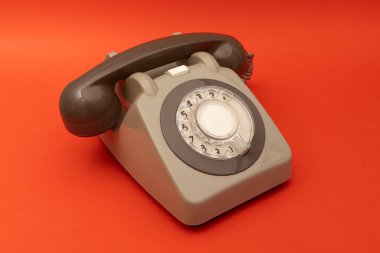 Canlı kırmızı bir arkaplan üzerine kurulmuş gri, eski bir döner telefon. Retro estetik, telefonun sessiz tonuna karşı koyuyor. Kalın, canlı arkaplanla, zamansız çekiciliğini vurguluyor..