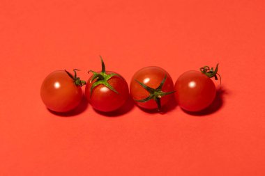Close-up of four ripe cherry tomatoes on a red background, emphasizing vibrant colors and natural texture. A minimalistic and aesthetic food composition perfect for culinary and healthy eating concept