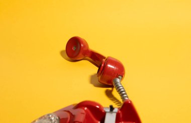Sarmalanmış kablosu olan klasik kırmızı bir telefon koyu sarı bir zemin üzerinde uzanır, nostalji ve klasik iletişimi çağrıştırır. Retro temalı tasarımlar, reklamlar ve yaratıcı projeler için mükemmel..
