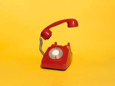 Kalın sarı arkaplanlı, kaldırılmış bir alıcısı olan kırmızı bir vintage telefon. Bu nostaljik görüntü klasik iletişimi, geçmişe dönük tarzı ve eski tarz teknolojiyi canlı bir kontrast ile temsil ediyor..