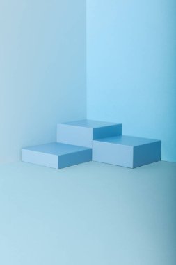 Mavi geometrik podyumların minimalist kompozisyonu tek renkli pastel mavi arka plana karşı merdiven benzeri bir formda düzenlenmiştir. Yumuşak ışıklandırma ve temiz tasarım modern, soyut ve estetik açıdan dengeli bir görsel yaratıyor..