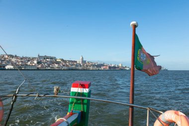 Lizbon 'un Tagus Nehri' ndeki manzarası Portekiz bayrağının dalgalandığı bir teknede çekildi. Tarihi şehir manzarası ve açık gökyüzü Portekiz 'in sahil cazibesini ve kültürünü gözler önüne seriyor..