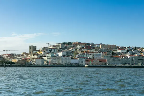 Lizbon 'un tarihi Alfama bölgesinin, Tagus Nehri' ndeki bir tekneden, berrak mavi gökyüzü altında geleneksel mimari ve renkli binalar sergilenen pitoresk bir manzarası..