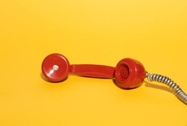 Canlı sarı arka planda klasik kırmızı telefon ahizesi. Cesur renklere sahip minimalist bir retro kompozisyon nostalji ve klasik iletişim temalarını çağrıştırıyor. Pop tasarım kavramları için mükemmel.