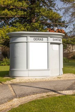 Portekiz 'in Oeiras kentindeki umumi tuvalette, boş bir reklam paneli ile kıvrımlı bir tasarım sergileniyor, sakin bir günde yeşil alanla çevrili ve parlak doğal ışıkla yıkanmış..