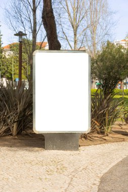 Lizbon parkındaki boş bir reklam panosu, yeşil ve kaldırım taşı yollarıyla çevrili, parlak bir şehir ortamında promosyon içeriği için temiz ve açık bir tuval sunuyor..