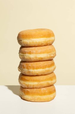 Beş jöleli donuttan oluşan mükemmel istiflenmiş bir kule, bej renkli bir zemin üzerinde duruyor, simetri, doku ve sıcak tonlarda temiz ve minimal besin fotoğrafçılığı içeriyor..