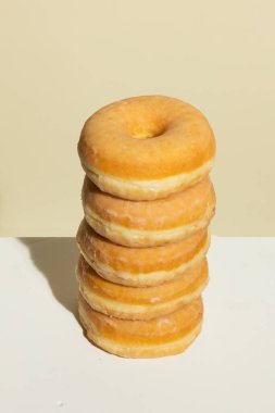Beş jöleli donuttan oluşan mükemmel istiflenmiş bir kule, bej renkli bir zemin üzerinde duruyor, simetri, doku ve sıcak tonlarda temiz ve minimal besin fotoğrafçılığı içeriyor..