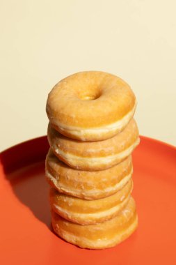 Kalın turuncu bir tabağın üzerinde, altı tane altın kaplamalı çörek duruyor. Sıcak tonlarla minimalist tasarımı görsel olarak dengeli ve iştah açıcı bir besin kompozisyonunda harmanlıyor..