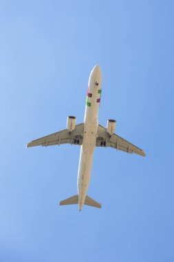 İniş ve kalkış sırasında çekilen iniş ve iniş takımlarını gösteren açık mavi gökyüzüne doğru uçan bir ticari uçağın alçak açılı görüntüsü..