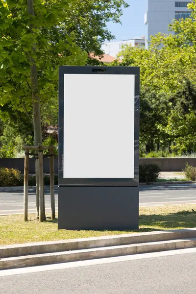 Şehir parkında güneşli bir günde dikey boş ilan panosu. Yeşillik ve şehir unsurlarıyla çevrili açık hava reklamları, modeller veya tanıtım içeriği için ideal..