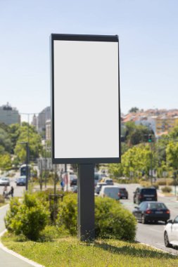 Portekiz 'in güneşli bir kentsel caddesinde boş dikey dijital ilan panosu. Arka planda açık mavi gökyüzü ve şehir mimarisi ile modelleme, reklam ve pazarlama tasarım sunumları için ideal.
