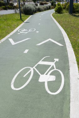 Yeşil asfalt bir yol üzerinde beyaz bisiklet sembolleri ve oklarla işaretlenmiş bisiklet yolu çimen ve bitki örtüsüyle çevrili, Portekiz 'de kentsel bisikletçiliği ve güvenli ulaşımı teşvik ediyor