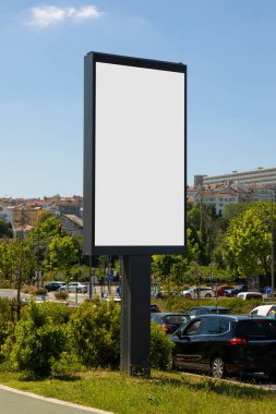 Portekiz 'in güneşli bir kentsel caddesinde boş dikey dijital ilan panosu. Arka planda açık mavi gökyüzü ve şehir mimarisi ile modelleme, reklam ve pazarlama tasarım sunumları için ideal.