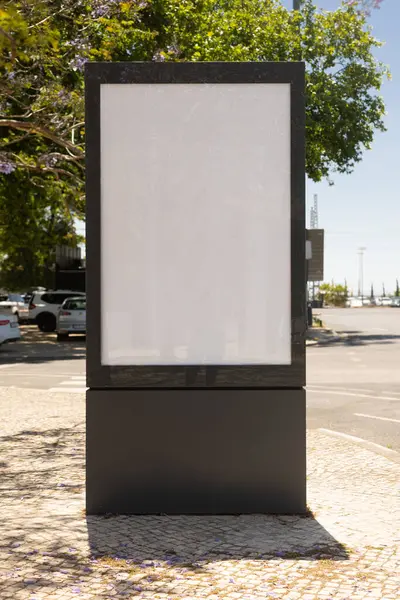 Güneşli bir Lizbon caddesinde dikey boş reklam panosu modeli kaldırımlı ve yapraklı ağaçlar, açık hava reklamcılığı ve poster tasarımı için mükemmel..