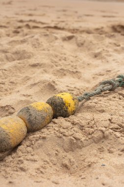 Kumsalda kısmen kumlara gömülü bir ipe bağlı sarı şamandıra. Yaz için ideal, sahil güvenliği, ya da dokulu, doğal bir geçmişi olan deniz temalı görseller..