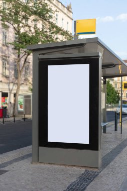 Günümüz otobüs durağında boş bir reklam panosu, güneşli bir öğleden sonra klasik binalar, hafif trafik ve ağaçlarla çevrili bir Avrupa şehrinin kaldırımında duruyor..