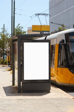 Şehir merkezinde güneşli bir günde modern bir tramvay durağında boş bir reklam panosu. Model, açık hava reklamı ya da toplu taşıma araçlarında markalaşma alanı.