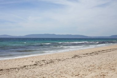 Portekiz 'in Comporta kentindeki huzurlu kumlu sahil, berrak turkuaz dalgalar ve uzaktaki Serra da Arrbida sıradağları. Alentejo 'da güneşli bir günde sakin kıyı manzarası.