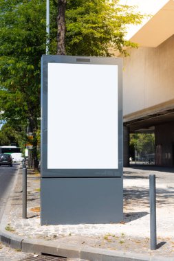 Güneşli bir günde beyaz ekranlı boş bir şehir reklam panosu modeli, reklam ya da tabelaya hazır. Ağaçlar, binalar ve geçen trafik ile çevrili bir şehir kaldırımında..