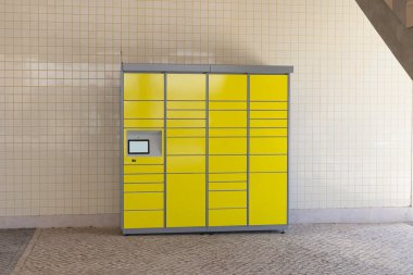 Kamu alanındaki fayanslı bir duvara monte edilmiş kişisel servis paketi ve teslimat için modern sarı paket dolabı..