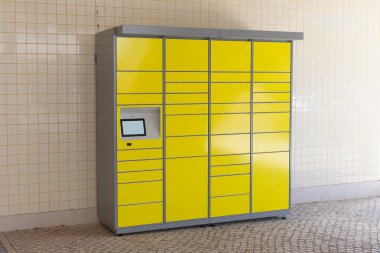 Kamu alanındaki fayanslı bir duvara monte edilmiş kişisel servis paketi ve teslimat için modern sarı paket dolabı..