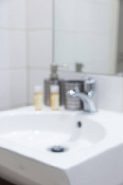 Modern banyo lavabosu krom musluk ve bulanık tuvalet eşyalarıyla dolu.