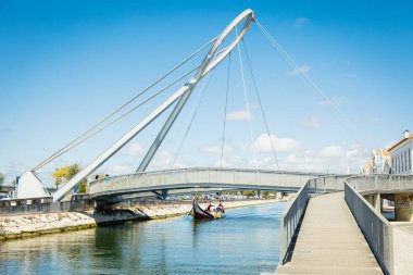 Turistler, Aveiro, Portekiz kanalları boyunca, 2025 tarihli renkli kurdelelerle kaplı köprünün yakınında tekne turnesinin keyfini çıkarıyorlar.