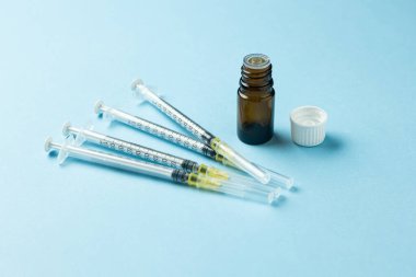 Açık kahverengi ilaç şişesi, beyaz kapaklı, açık mavi arka planda tek kullanımlık birkaç şırınganın yanında. Aşı, tıbbi tedavi veya ilaç tedavisi kavramı.