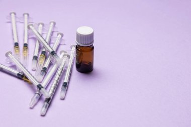 İğneli tıbbi şırıngalar küçük kehribar bir cam şişenin etrafına saçılmış..