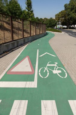 Trafik işaretleri ve verim işaretleriyle yeşil bisiklet yolu, güneşli bir günde bir yaya geçidinin yanında..