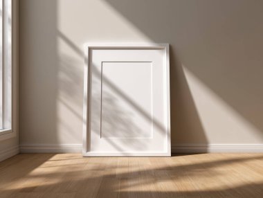 Beyaz bir çerçevenin minimalist bir maketi bej bir duvara yaslanmış, yumuşak doğal güneş ışığı ve ahşap zemine düşen gölgeler. Modern ve zarif bir ortamda poster, fotoğraf ya da sanat eserleri sergilemek için mükemmel..