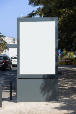 Lizbon, Portekiz 'de bir kaldırımda dikey boş reklam panosu. Arka planda binalar ve yeşillik olan bir yolun yanında..