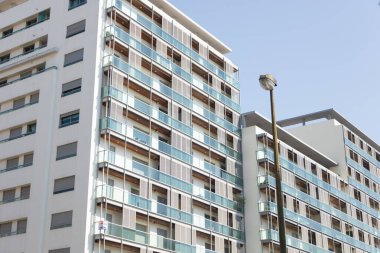 Açık mavi gökyüzünün altında balkonları olan modern apartmanlar.