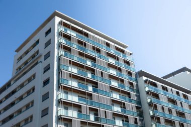 Cam balkonları ve çağdaş mimari tasarımı olan modern bir apartman dairesi, açık mavi gökyüzü altında çekildi. Temiz hatları, geniş pencereleri ve minimalist cepheli kentsel konutlar