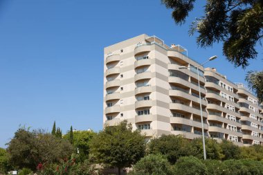 Lizbon 'da, kıvrımlı balkonları, açık renkli cephesi olan ve ağaçlarla çevrili modern bir apartman dairesi. Fotoğraf açık, güneşli bir günde, açık mavi gökyüzü ile çekildi..