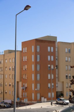 Açık mavi gökyüzünün altında sarı duvarları ve modern pencereleri olan apartman cephesi.