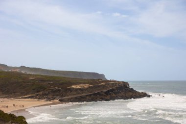 Portekiz, Praia das Mas 'ta kayalık kıyı şeridi ve okyanus dalgaları. Uçurumlar, sahil ve deniz kenarındaki parlak gökyüzü altında Atlantik kıyısının manzarası. Seyahat, turizm ve doğa kavramları için mükemmel bir imaj..