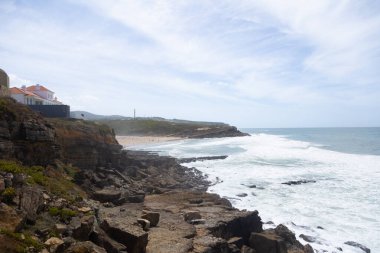 Portekiz, Praia das Mas 'ta kayalık kıyı şeridi ve okyanus dalgaları. Uçurumlar, sahil ve deniz kenarındaki parlak gökyüzü altında Atlantik kıyısının manzarası. Seyahat, turizm ve doğa kavramları için mükemmel bir imaj..