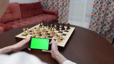 Çevrimiçi satranç. Yeşil ekranlı telefon arka planda satranç tahtası. Hobi ve eğitim. Kadın telefonu tutuyor. Yüksek kalite 4k görüntü