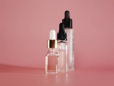 Pembe arka planda serumu ve pipeti olan şeffaf üç kavanoz. Kozmetik ve güzellik. Kişisel bakım. Cilt bakım ürünleri reklamı, lüks kozmetik ürünleri, parlayan madde özü damlası. Güzellik