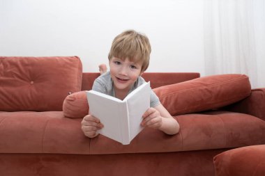 Bebek kanepede uzanıyor, kitap okuyor ve kameraya bakıyor. Sevimli çocuk kitabın arkasından dışarı bakıyor. İlginç bir çocuk kitabı. Market çocuğu. Çocuk gelişimi. Yüksek kalite fotoğraf